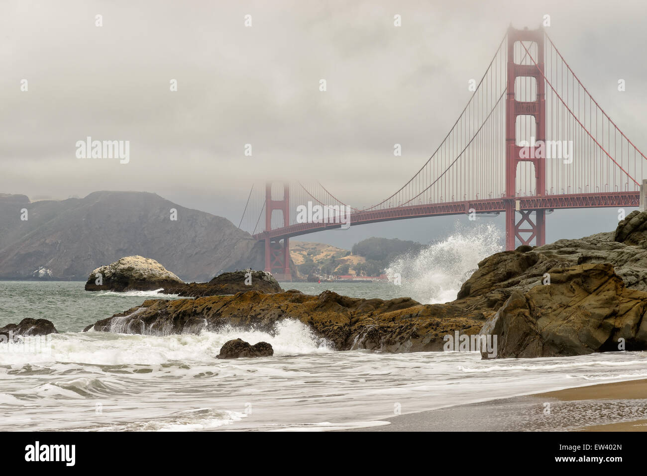 Schwarzen Felsen und Meer Wellen am Baker Beach wie Golden Gate Bridge im Nebel auf Hintergrund in San Francisco, USA. Stockfoto