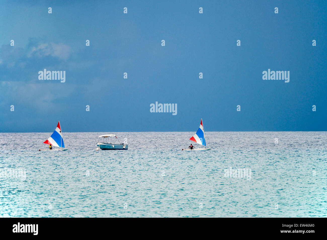 Zwei kleine Segelboote Segeln vorbei an einem verankerten Motorboot in der Karibik, mit stürmischen Himmel. Stockfoto
