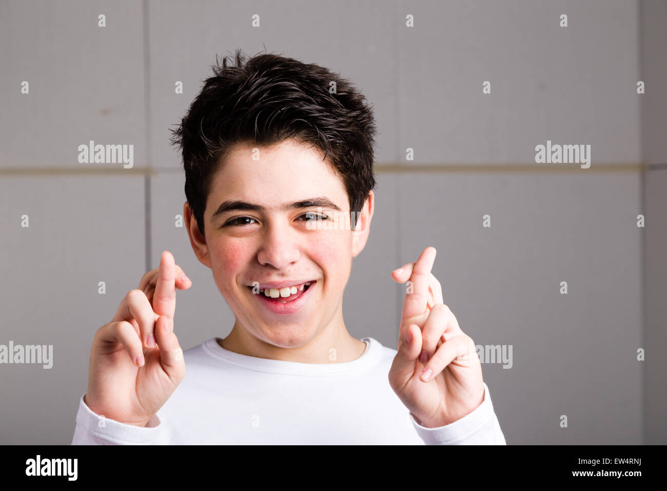 Lateinische junge mit Akne in eine weiße Langarm T-shirt lächelt Daumen beider Hände als abergläubische Geste um Glück auf industriellem Hintergrund Stockfoto