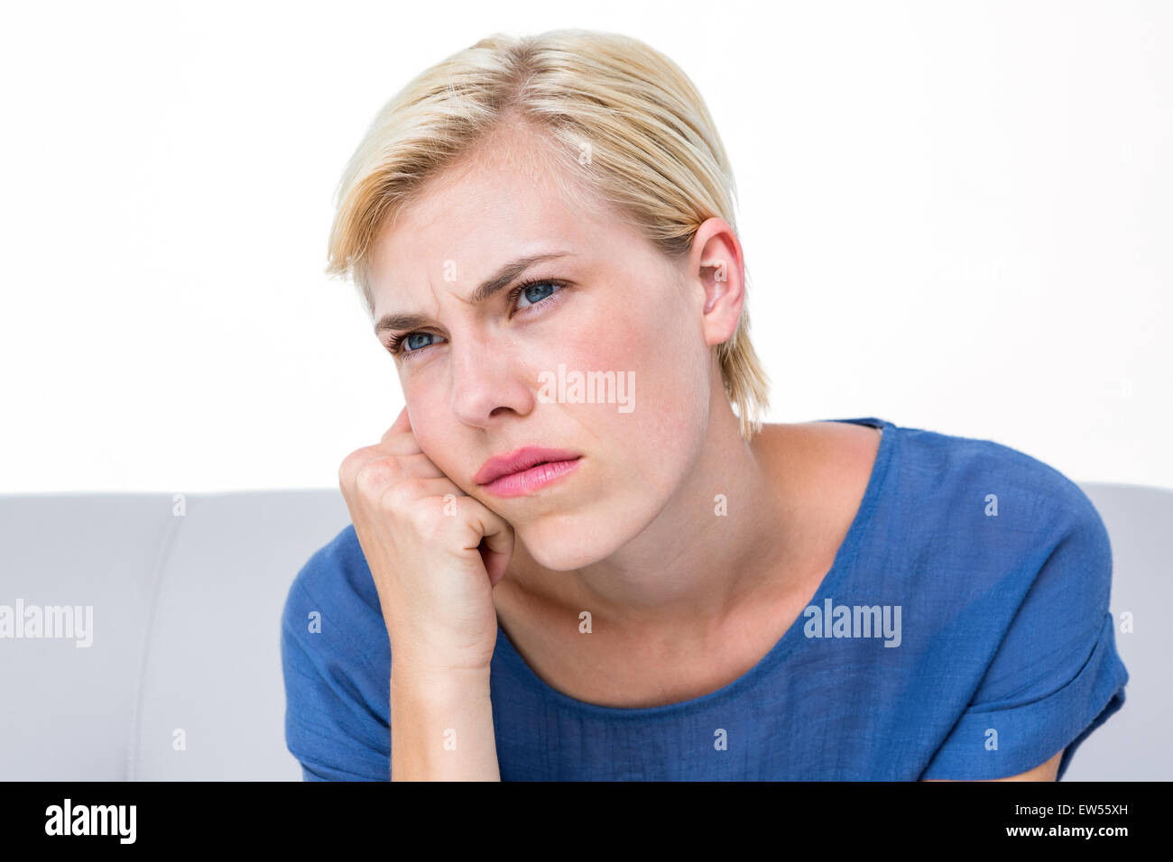 Nachdenkliche blonde Frau sitzt auf der couch Stockfoto