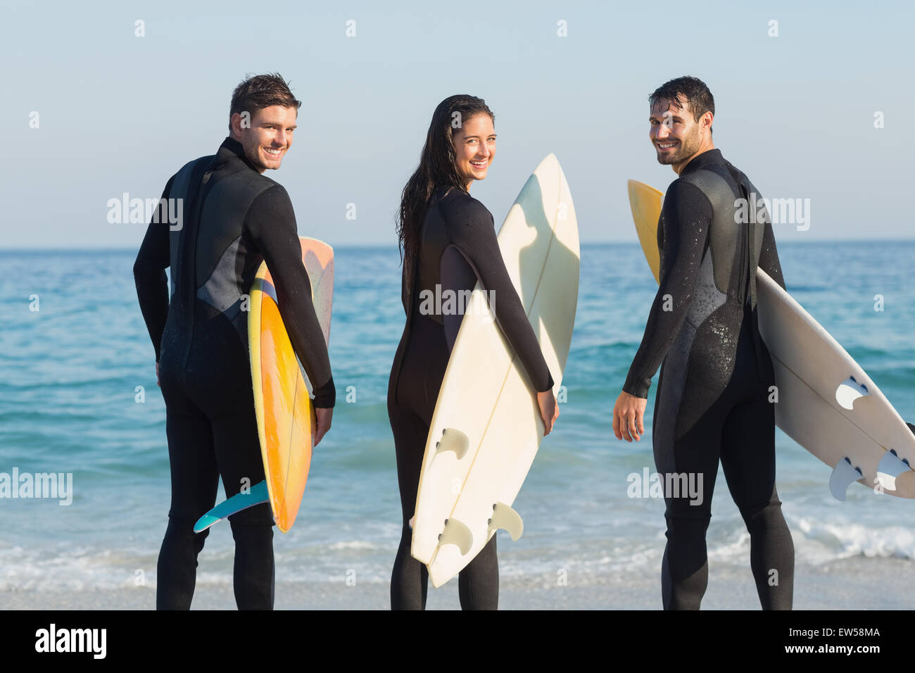 Gruppe von Freunden auf Neoprenanzüge mit einem Surfbrett an einem sonnigen Tag Stockfoto