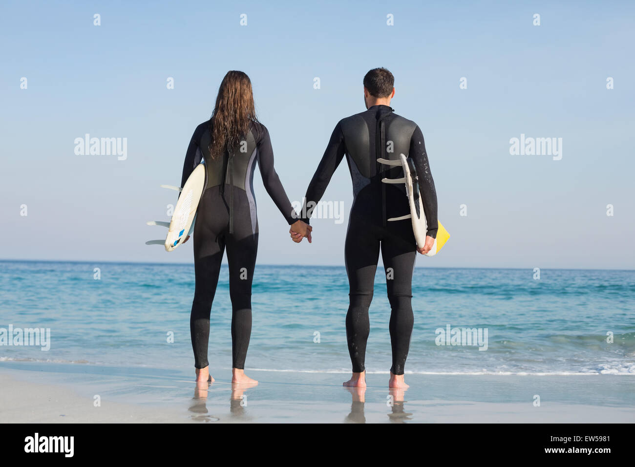 glückliches Paar in Neoprenanzüge mit Surfbrett an einem sonnigen Tag Stockfoto