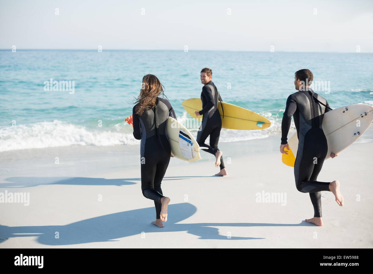 Gruppe von Freunden auf Neoprenanzüge mit einem Surfbrett an einem sonnigen Tag Stockfoto