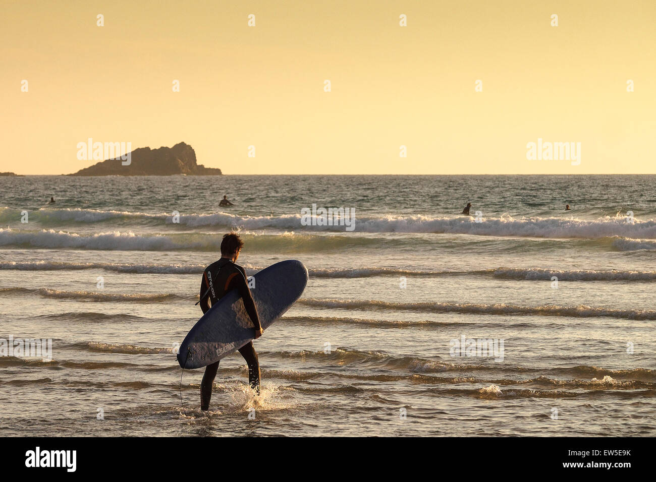 Ein Surfer, der beim Sonnenuntergang über dem Fistral Beach in Newquay, Cornwall, ins Meer geht. VEREINIGTES KÖNIGREICH. Stockfoto