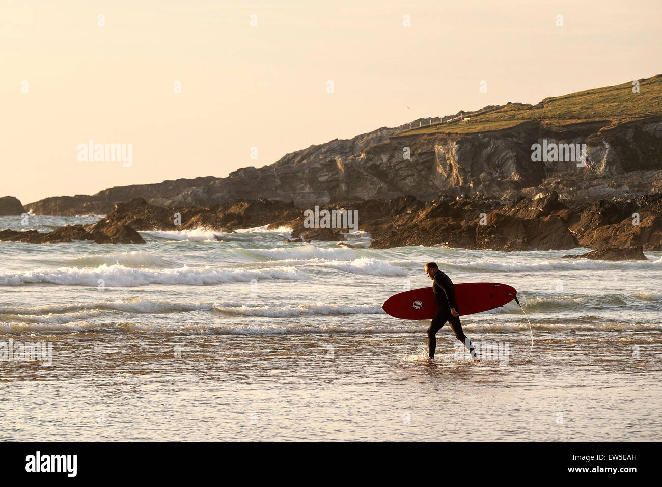 Eine Surfer trägt seinem Surfbrett, wie er am Fistral ins Meer geht. Stockfoto