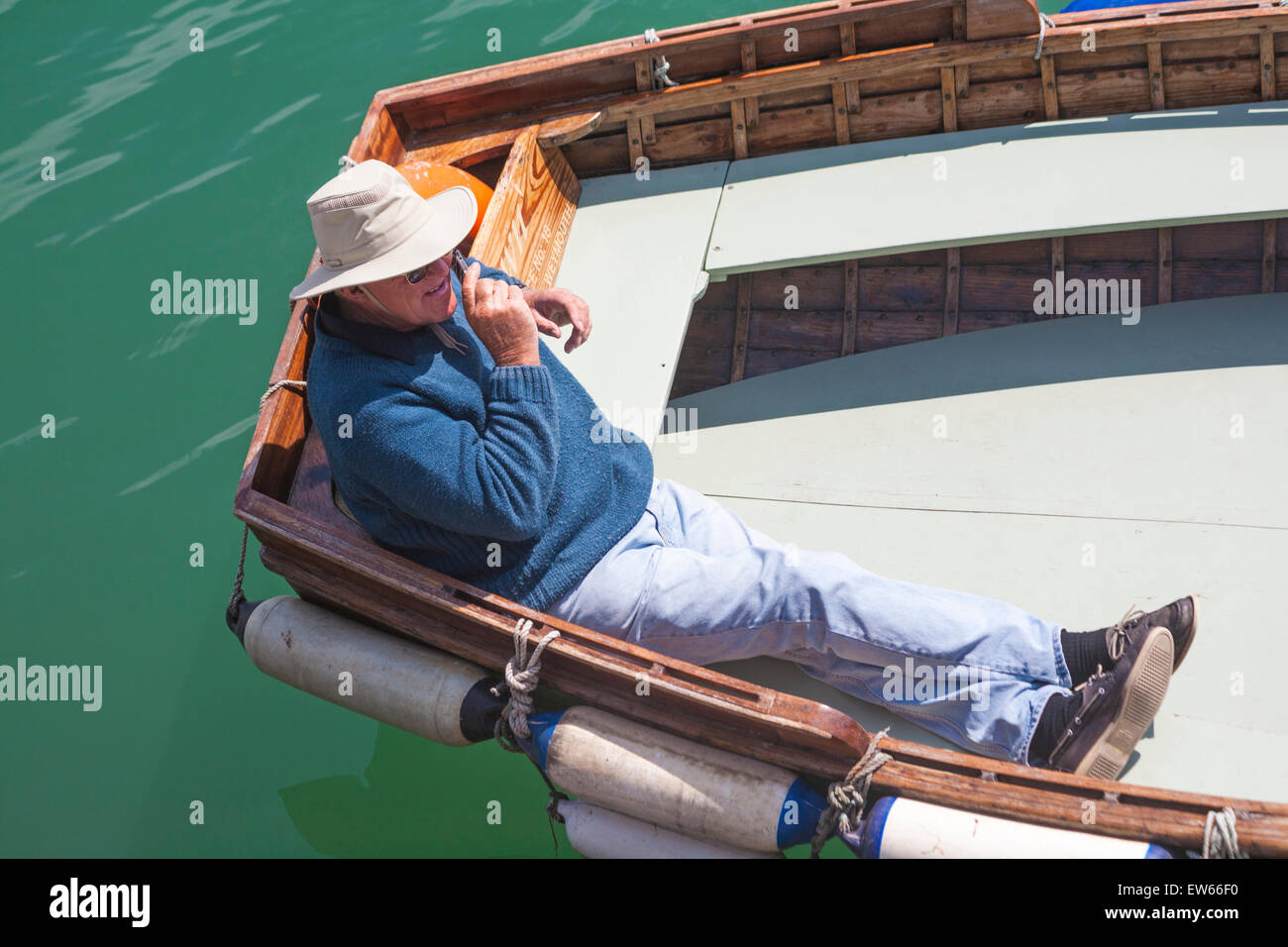 Ferry Mann auf der Handy-relaxen am Ruderboot in der Sonne warten auf Passagiere bei Weymouth, Dorset im Juni Stockfoto