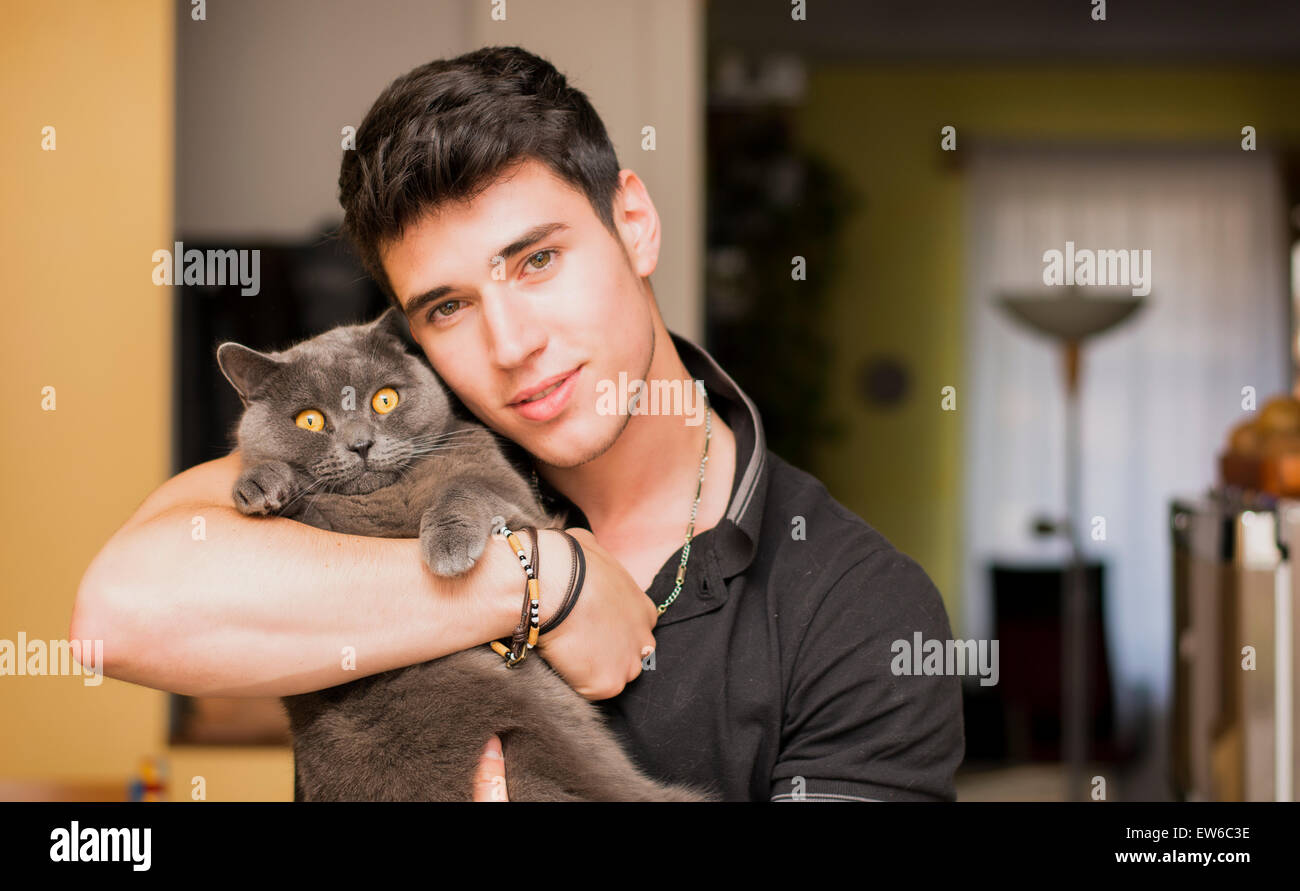 Hübscher Junge Tierliebhaber Mann innen the House, umarmt seine graue Katze-Haustier. Stockfoto