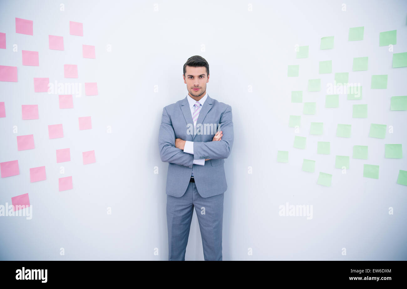 Gut aussehend Geschäftsmann mit Arme gefaltet Stand in der Nähe der Wand mit Aufklebern im Büro Stockfoto