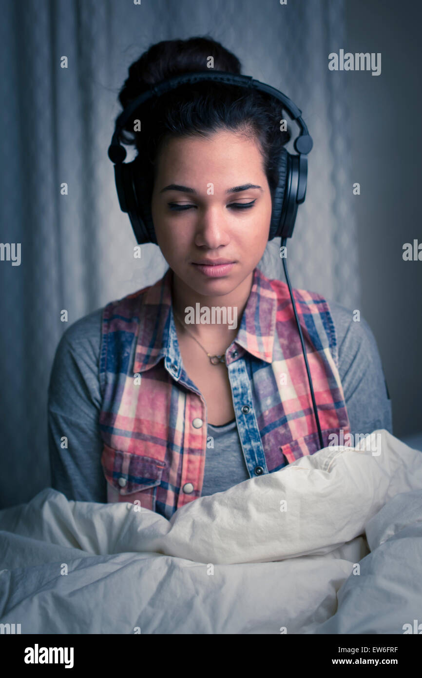 Eine junge Frau hört Kopfhörer in ihrem Zimmer unter der Bettdecke. Stockfoto
