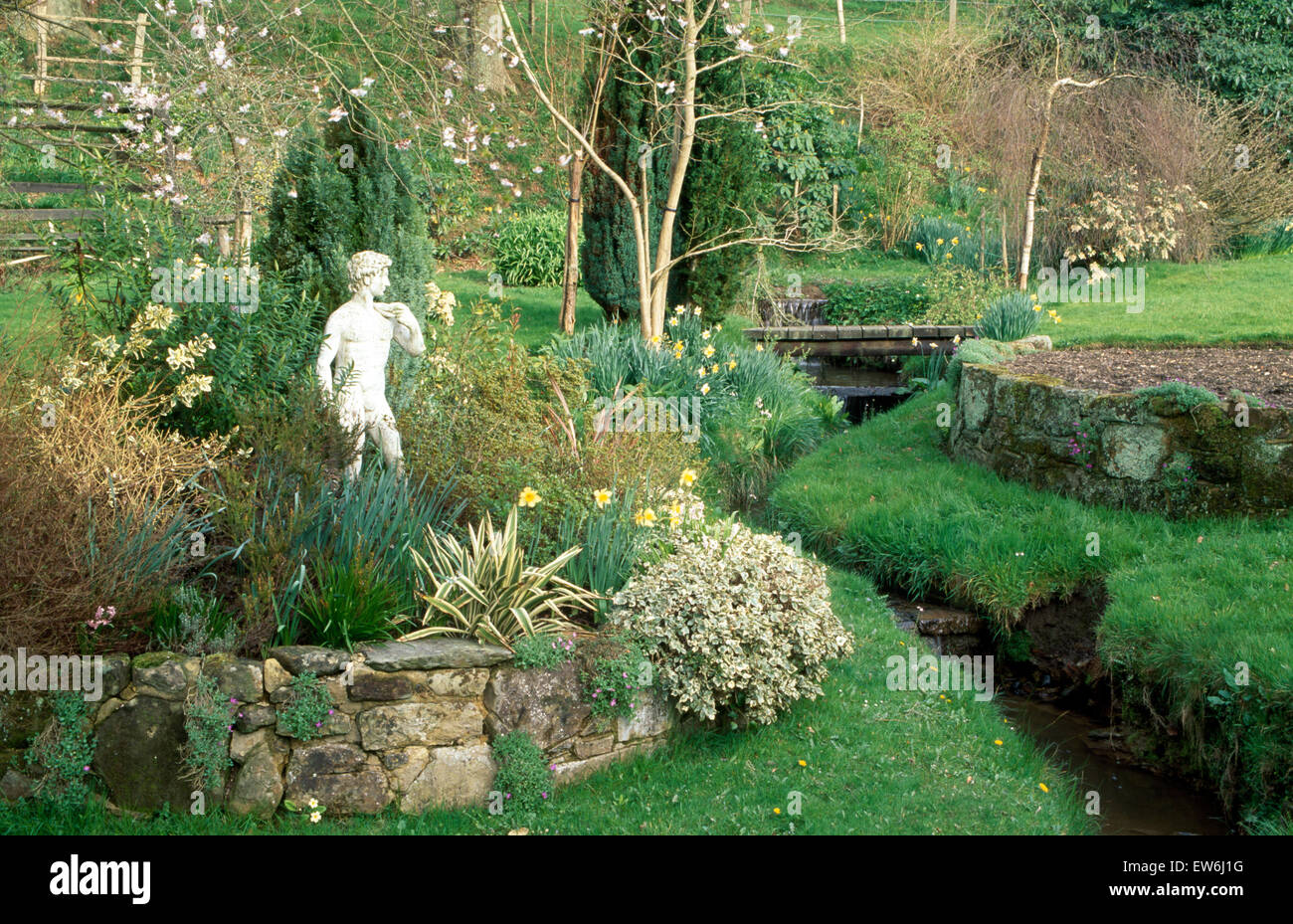 Klassische Statue im Hochbeet neben kleinen Bach im großen Garten im Frühjahr Stockfoto