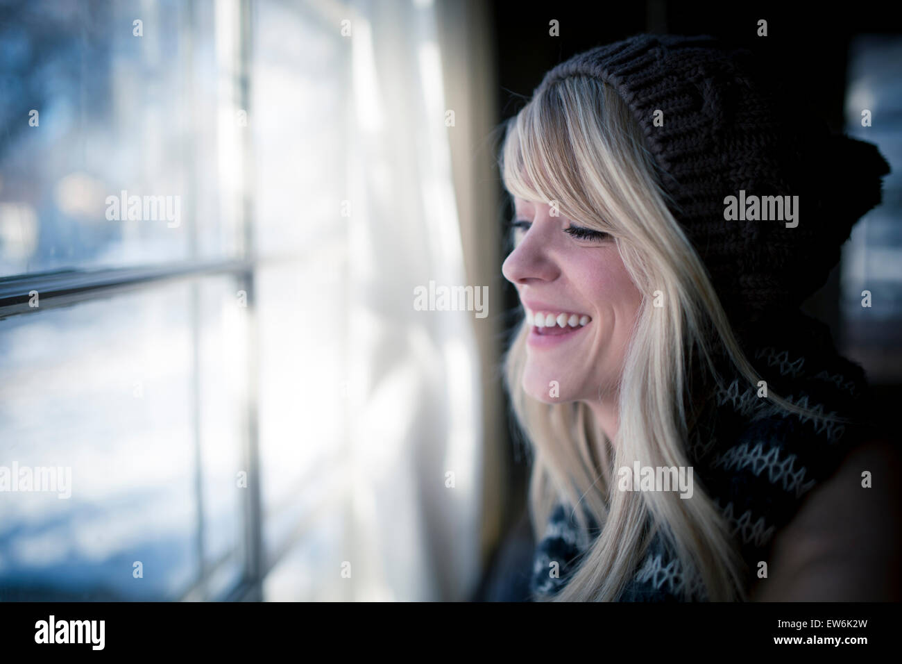 Eine junge Frau schaut ein Fenster lächelt. Stockfoto