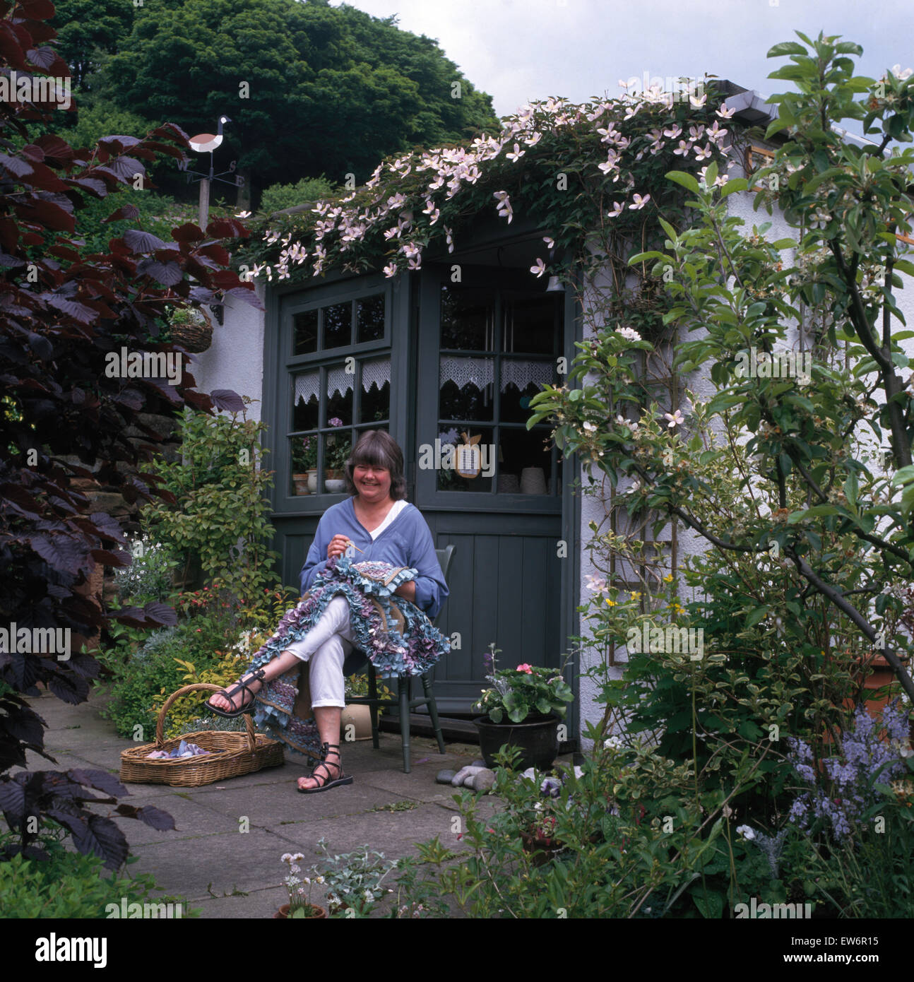 Porträt der lächelnde Frau sitzen und Nähen vor Hütte Tür Stockfoto