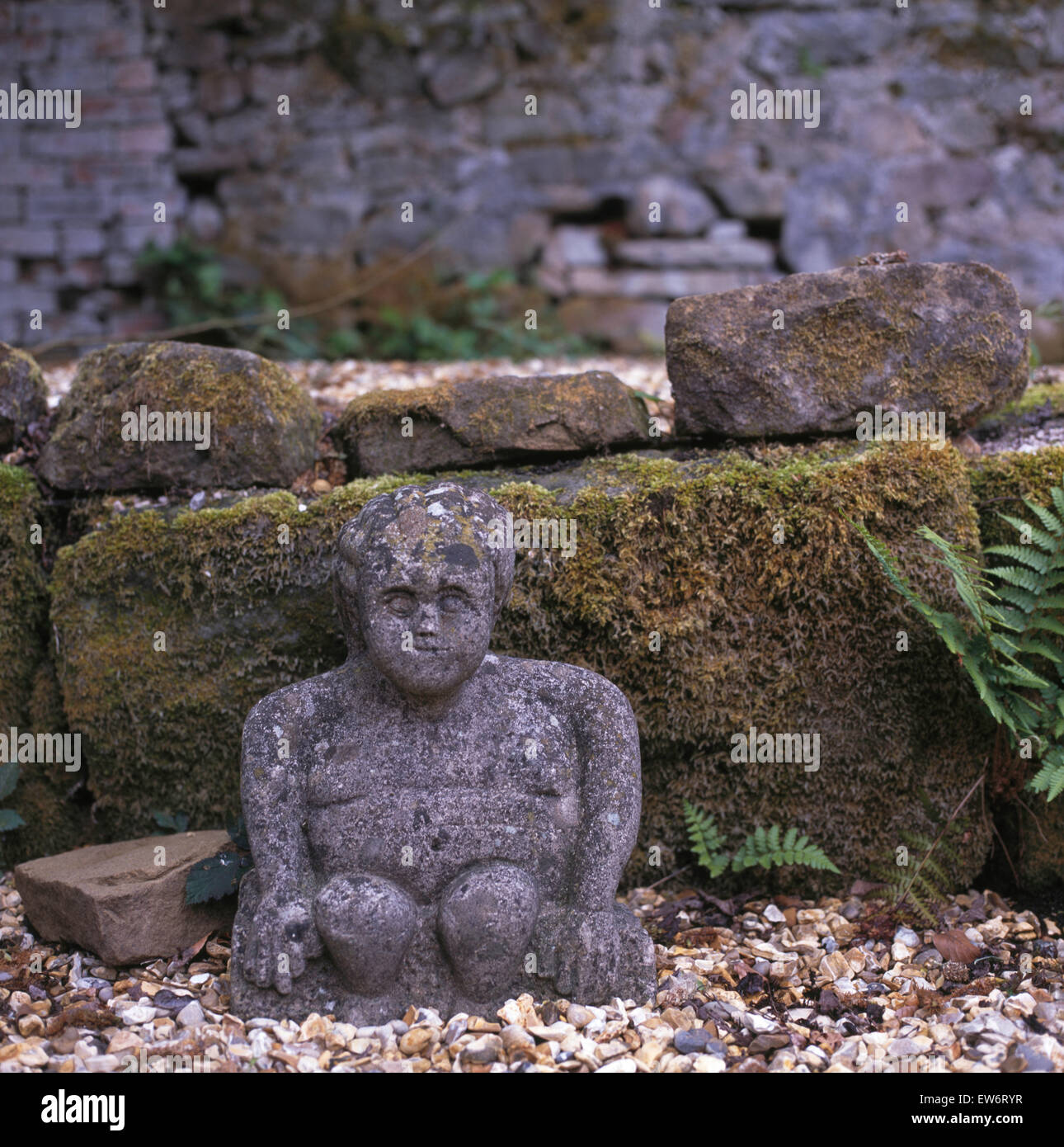 Verwitterte Statue aus Stein neben moosigen Steinmauer im Garten Stockfoto