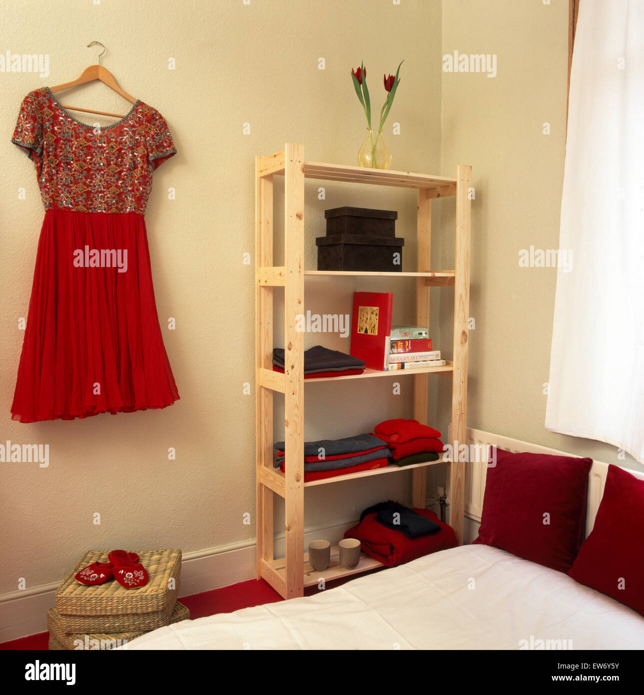 Rotes Kleid hängt an der Wand neben einfachen Holzregale in neunziger Jahre Wirtschaft Schlafzimmer Stockfoto