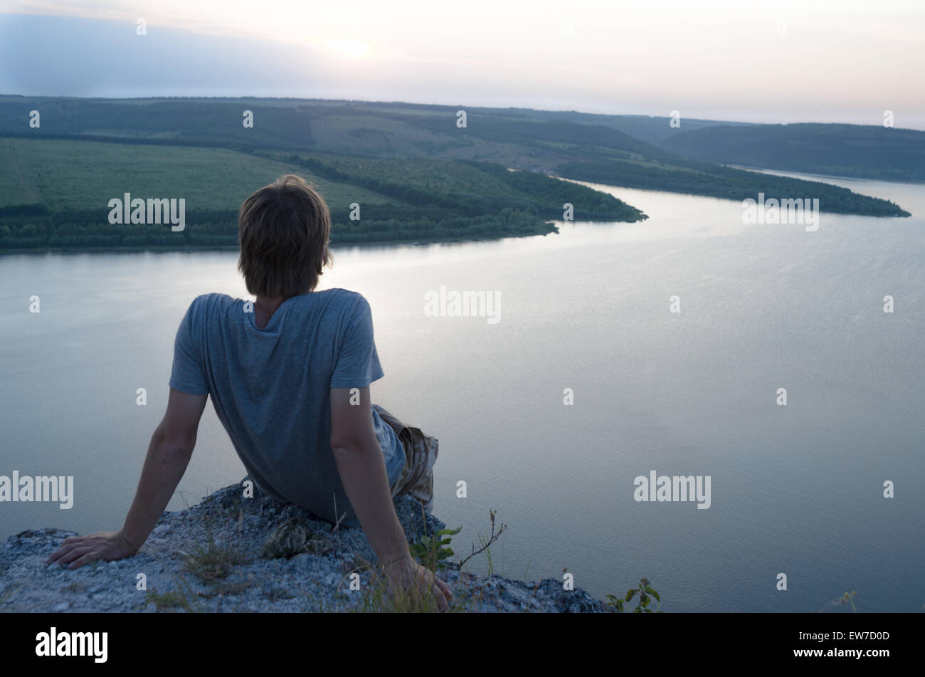 Mann sitzt auf einem Felsen über dem Fluss bei Sonnenuntergang, Reise-Konzept. Stockfoto