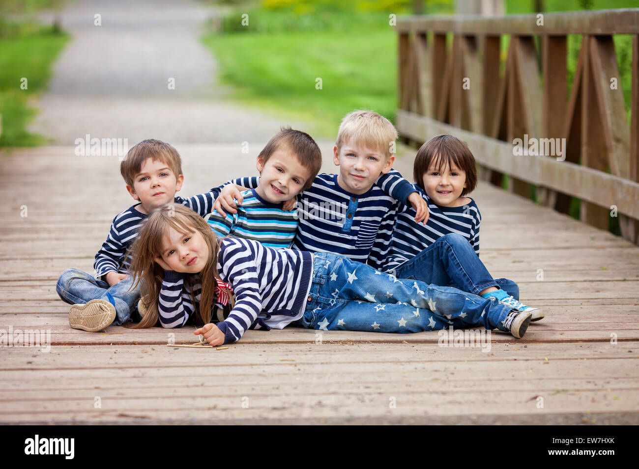 Fünf bezaubernde Kinder, gekleidet in gestreiften Hemden, sitzen auf einer Brücke im Park, Spaß Stockfoto