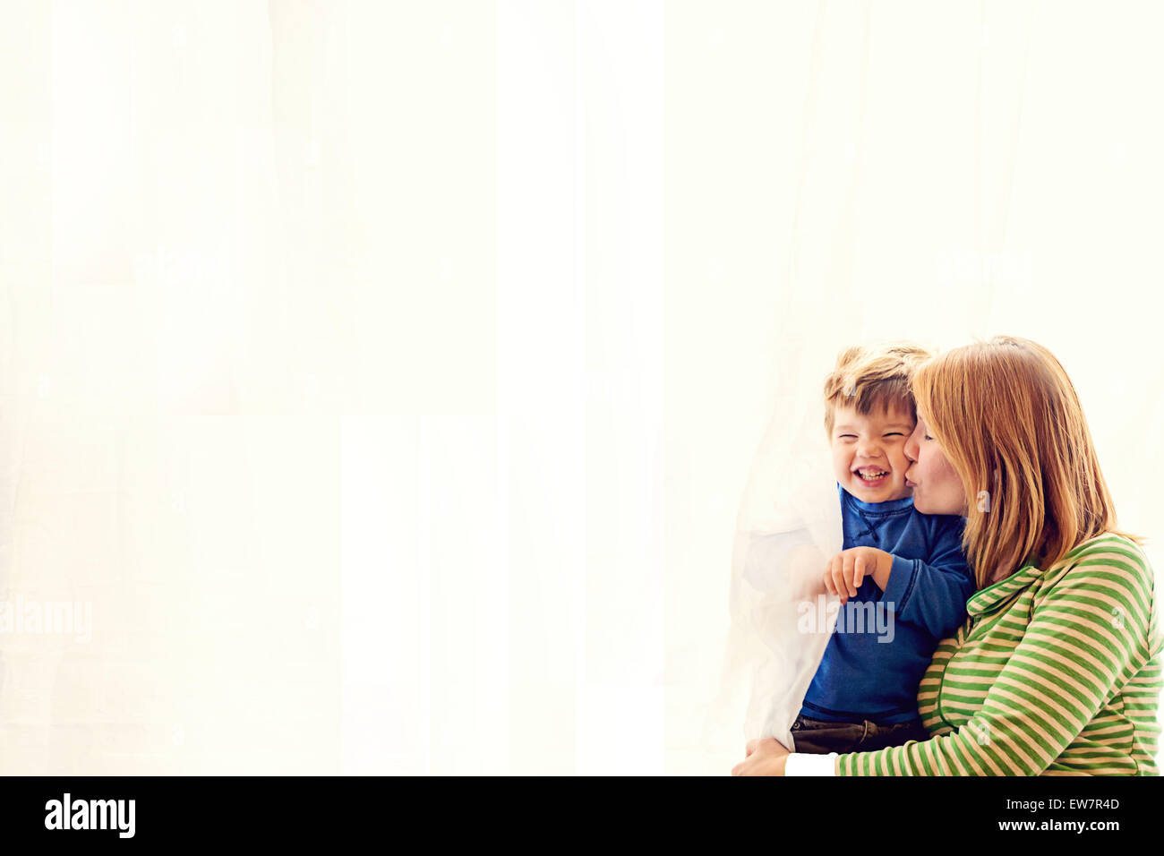 Mutter steht an einem Fenster und küsst ihren Sohn Stockfoto