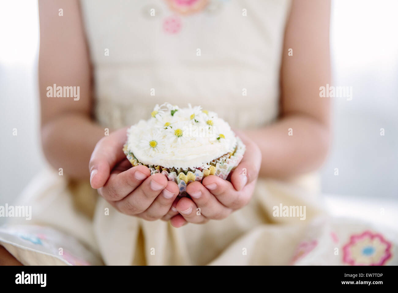 Mädchen hält Cupcake mit Gänseblümchen verziert Stockfoto
