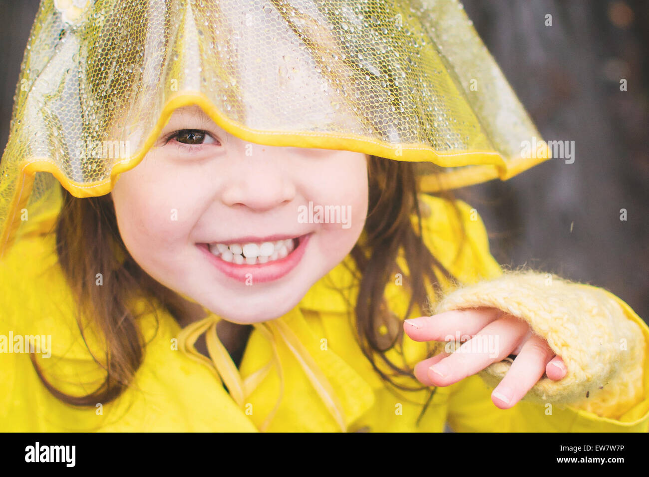 Lächelndes Mädchen trägt gelben Regenmantel und Hut Stockfoto