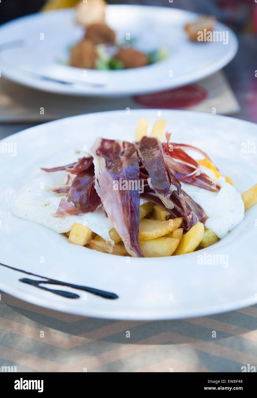 Stillleben mit weiße Schale mit typisch Spanien Essen benannt Huevos Rotos oder gebrochenen Eiern mit Kartoffeln Pommes frites gebratenen Eiern und sli Stockfoto