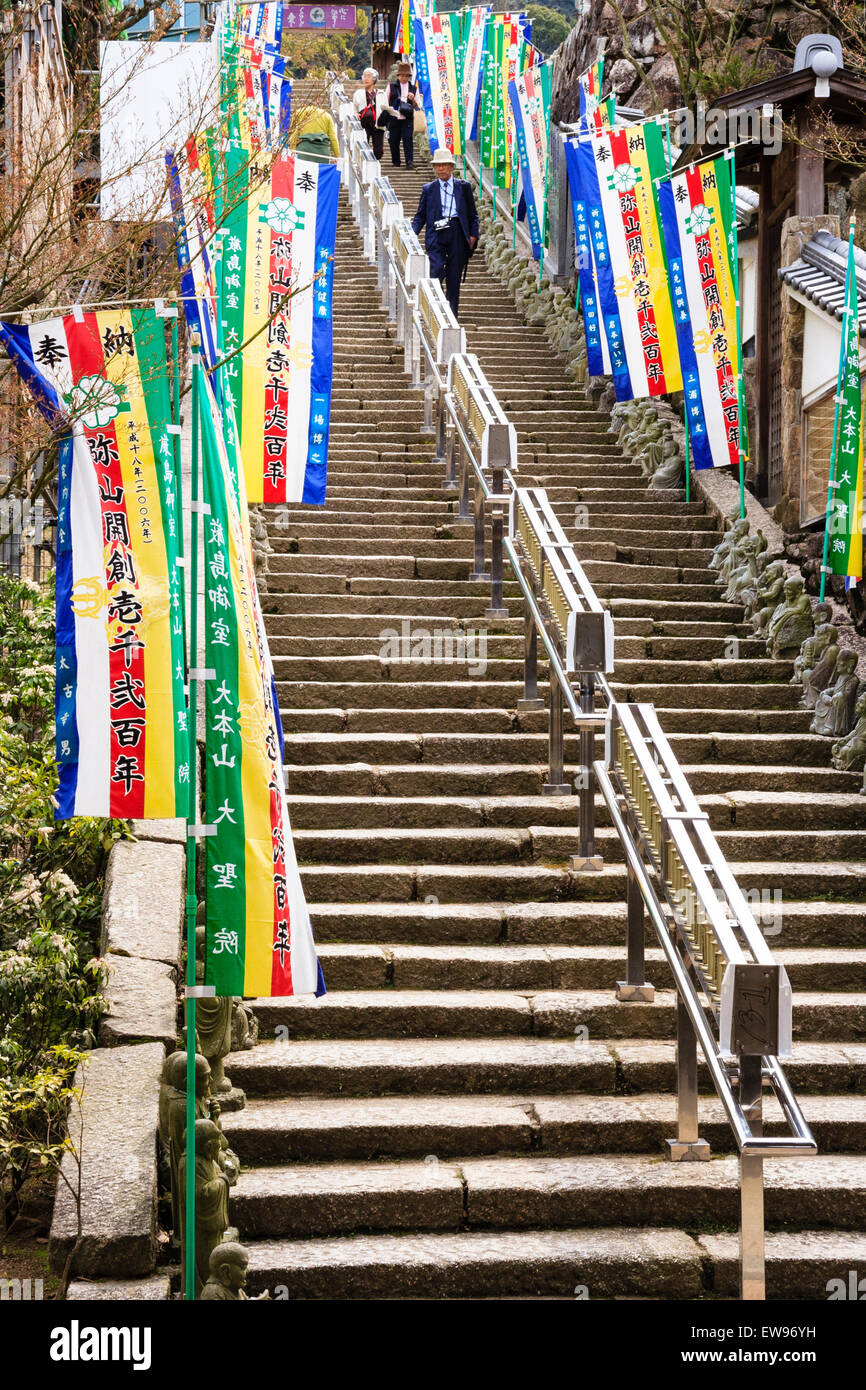 Japan, Miyajima, Daisho-in-Tempel. Doppelflug von Stufen vom Torhaus zum Tempel mit Rakan-Statuen buddhistischer Mönch und seitlichen Bannern. Stockfoto