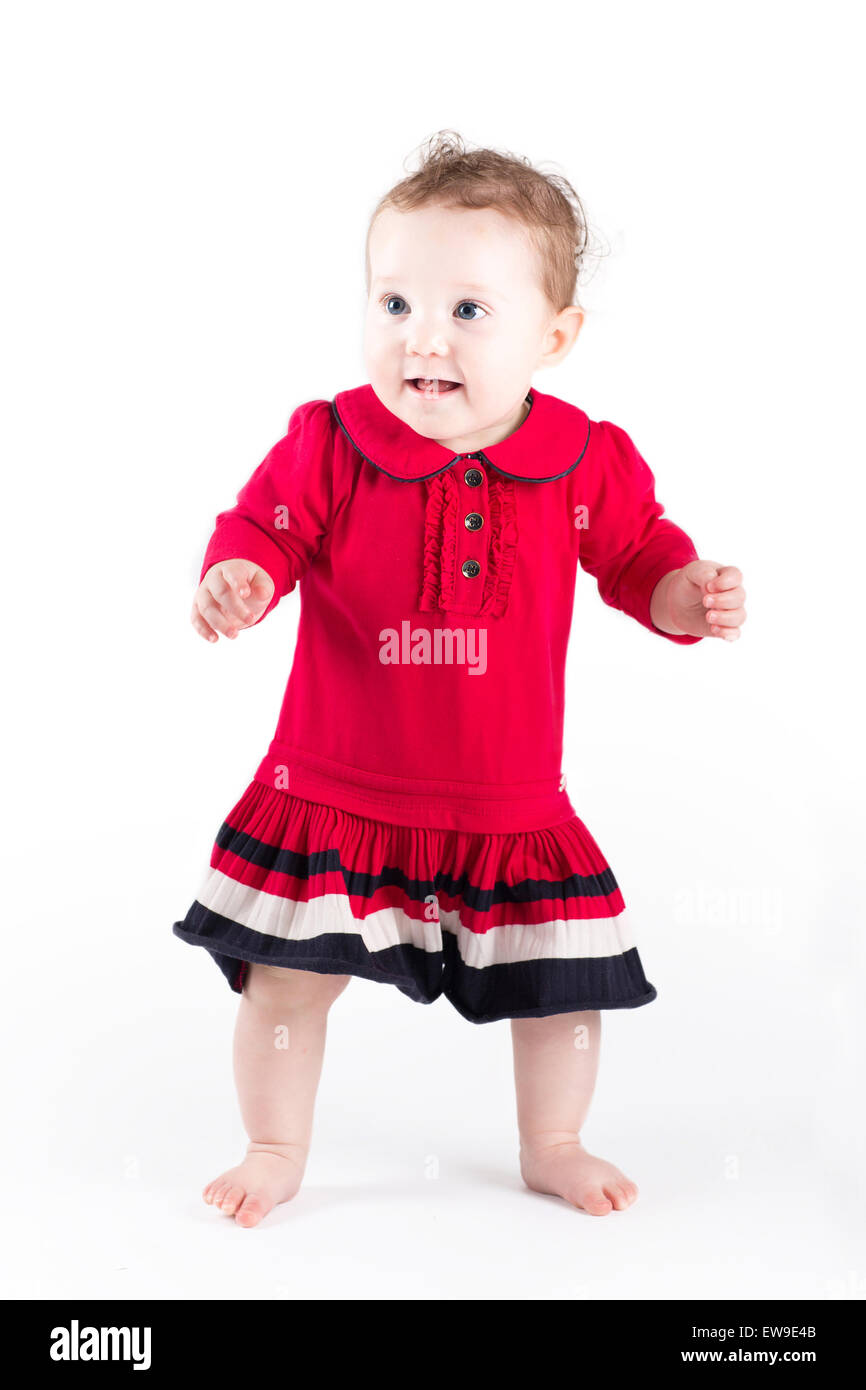 Süße Babymädchen in einem roten Kleid machen ihre ersten Schritte Stockfoto