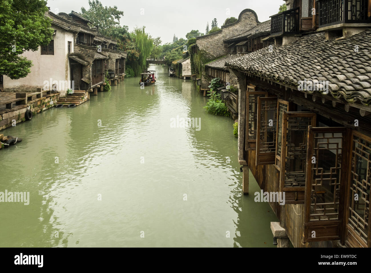 Steinbrücke und Gondel auf dem Kanal, der zwischen traditionellen chinesischen Häusern in der historischen malerischen Wasserstadt Wuzhen, China, verläuft Stockfoto