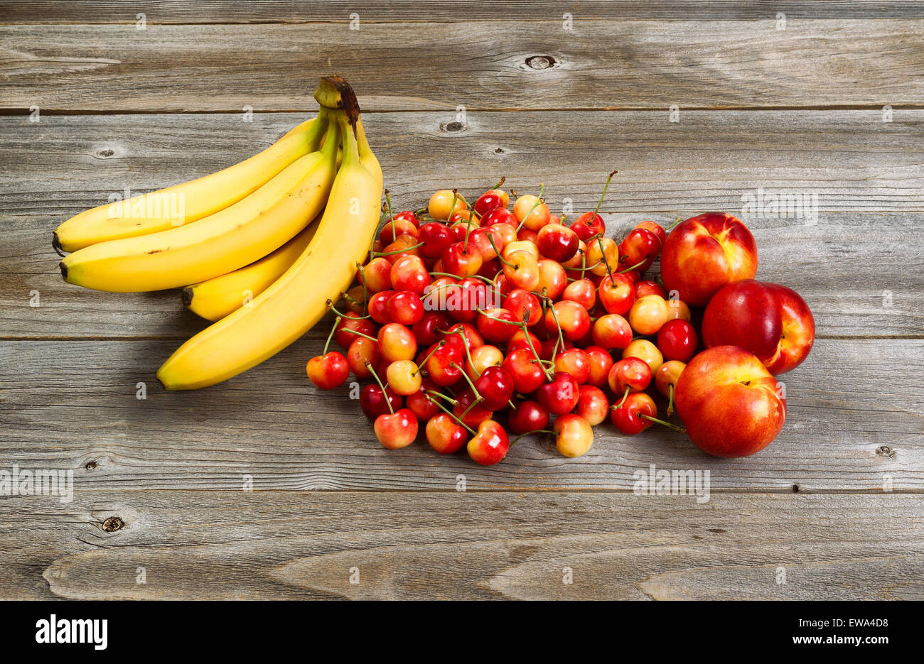 Frische reife Früchte bestehend aus Kirschen, Pfirsiche und Bananen auf rustikalen Holz. Stockfoto