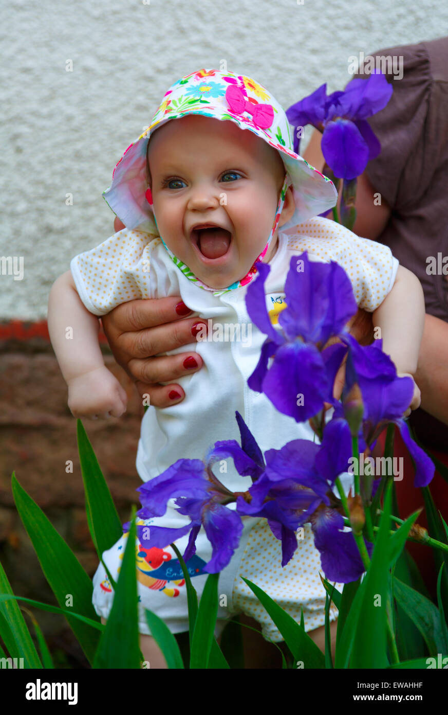 Das Fünf-Monats-Mädchen lacht fröhlich in der Nähe der blauen Schwertlilien Stockfoto