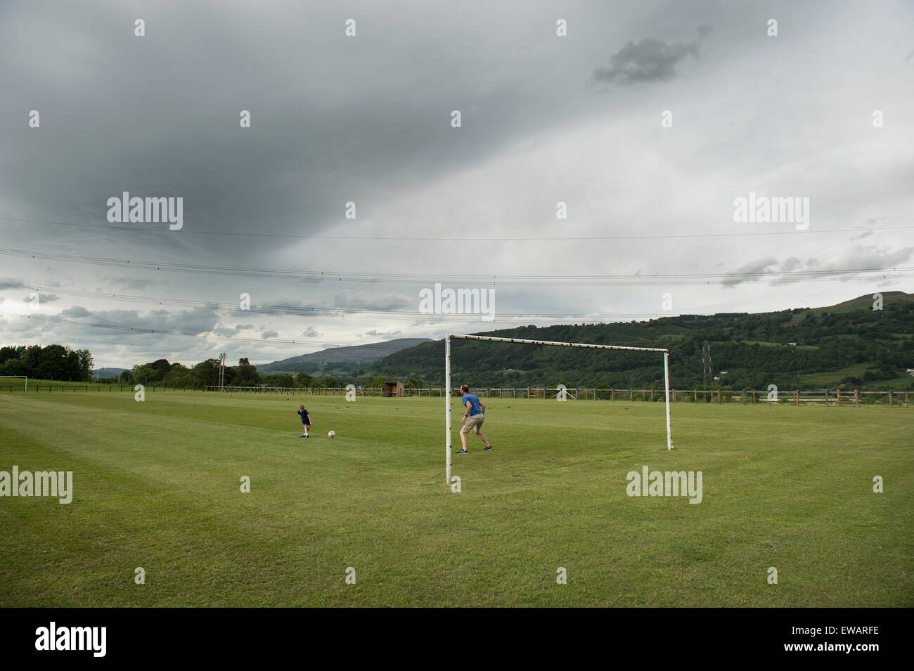 Ein kleiner Junge und ein Mann Fußball spielen auf einem bewölkten Tag in Wales Stockfoto