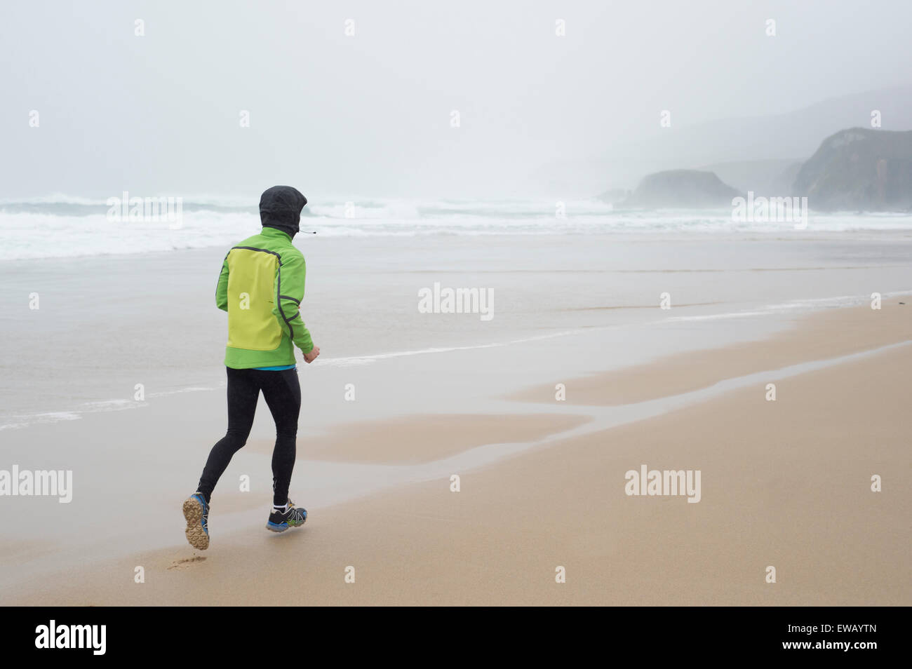 Läufer-Mann läuft am Strand an einem regnerischen Tag Stockfoto