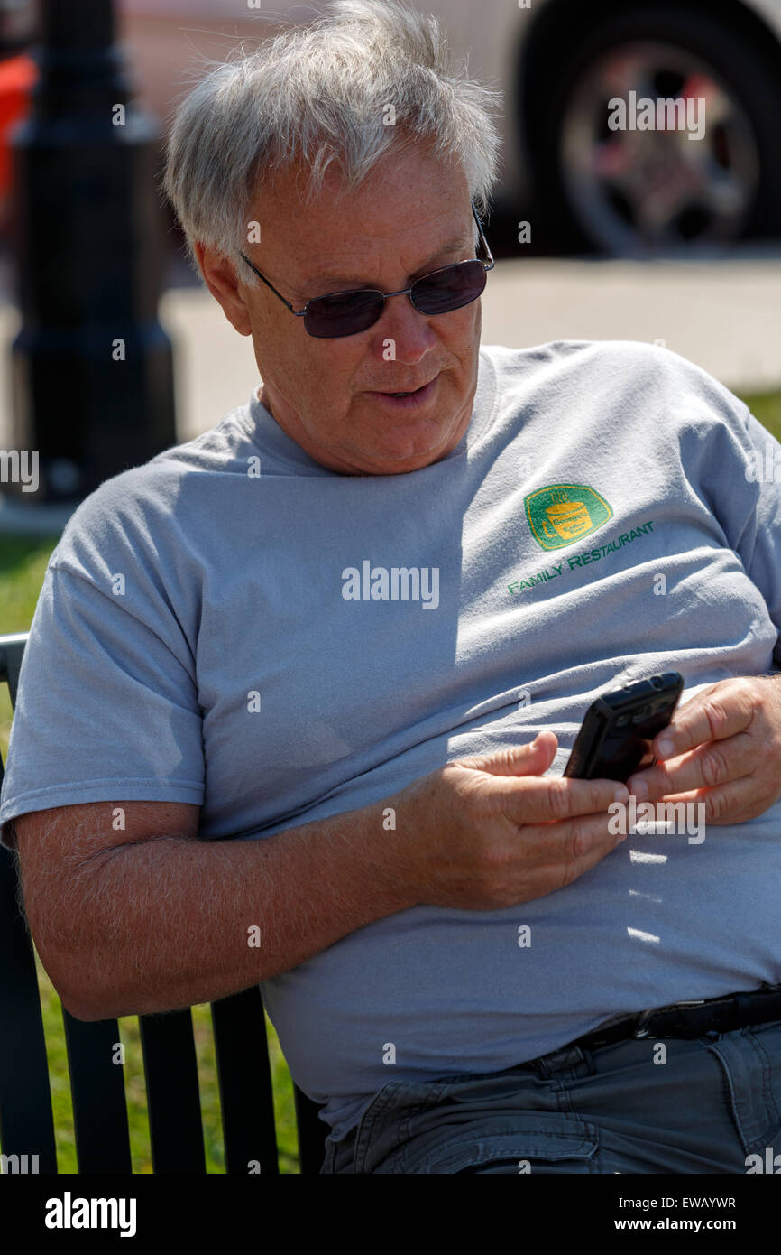 Ältere Männchen sitzen in der Sonne-SMS auf seinem Handy Stockfoto