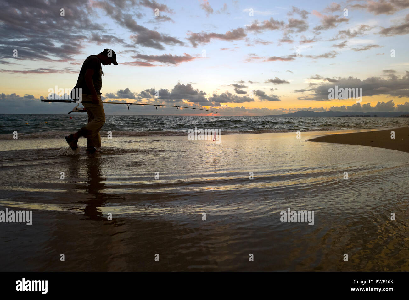 Fischer-Strand zu Fuß mit Angelrute und Sonnenuntergang im Hintergrund. Stockfoto