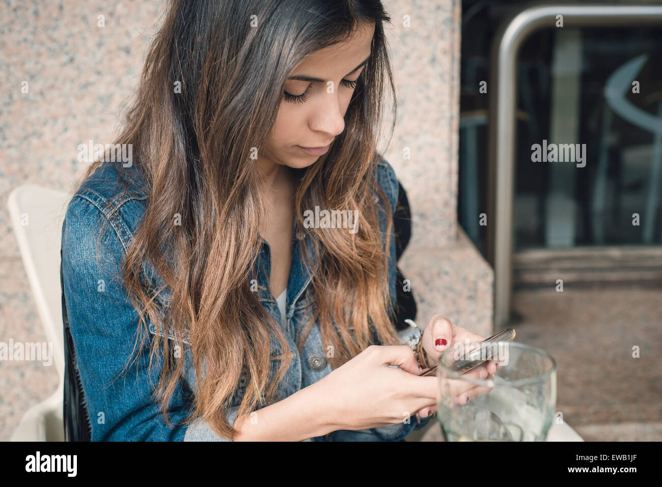 Brünette Frau eine SMS mit ihrem Smartphone. Frau nimmt einen Drink auf der Terrasse einer Bar. Stockfoto