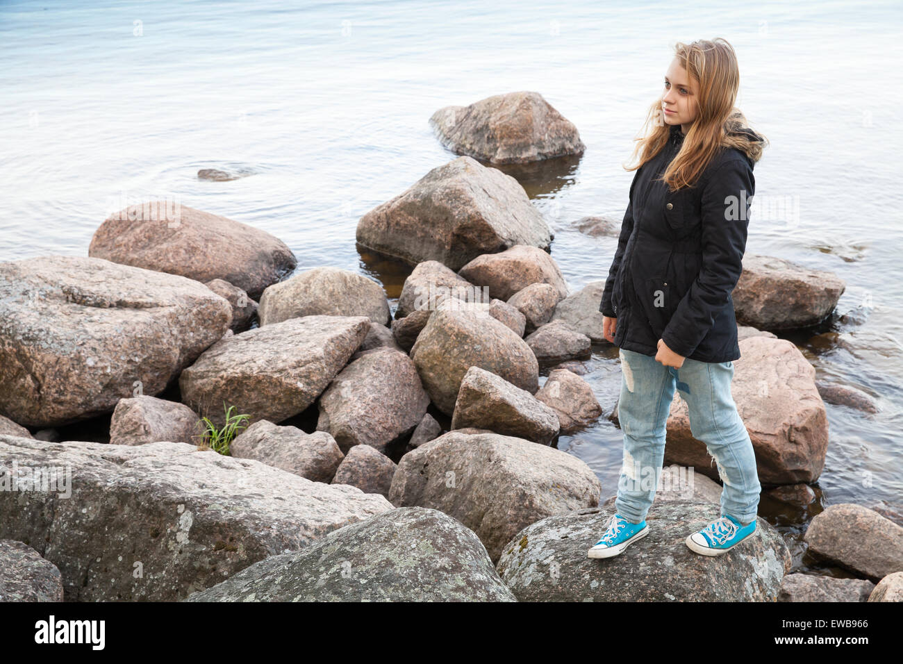 Schöne blonde kaukasische Teenager-Mädchen zu Fuß auf den Küsten Steinen entlang der See in Finnland Stockfoto