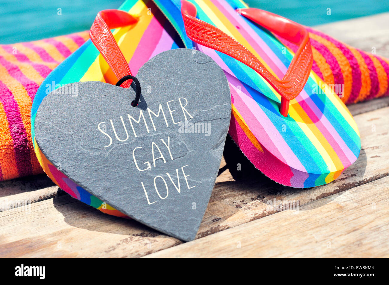 lieben Sie der Satz Sommer Homosexuell in einem herzförmigen Schiefer und ein paar Regenbogen Flip Flops und ein Strandtuch auf einem Brett geschrieben Stockfoto