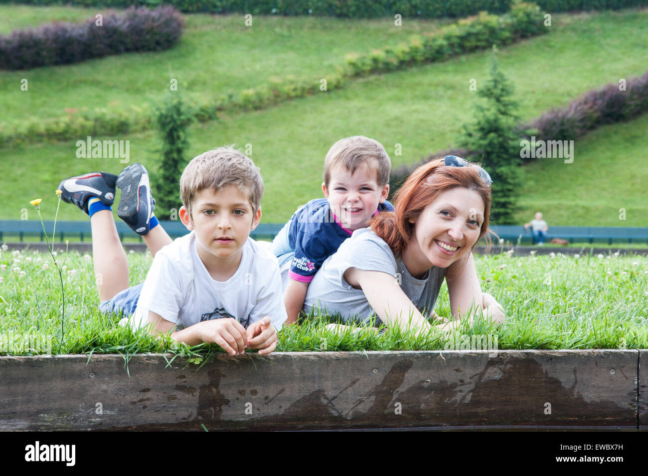 Porträt der Mutter mit zwei Kindern liegen auf dem Rasen am Ufer eines Teiches Stockfoto