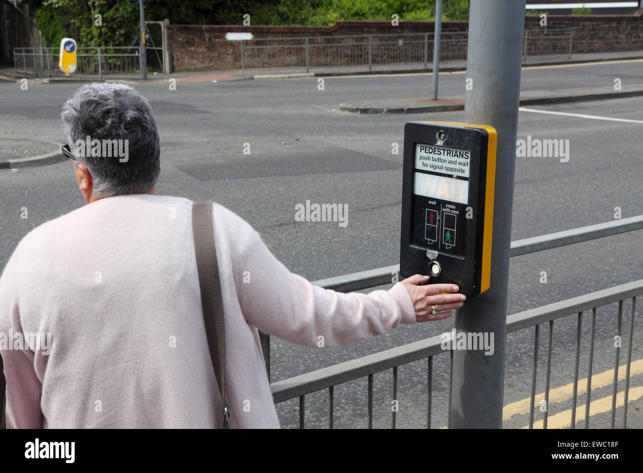 Frau mittleren Alters durch Betätigen der Taste für Fußgängerüberweg, UK Stockfoto