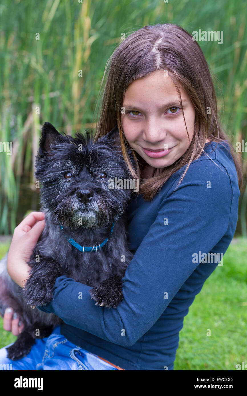 Kaukasischen Mädchens tragen und umarmt schwarzen Hund auf Arm in der Natur Stockfoto