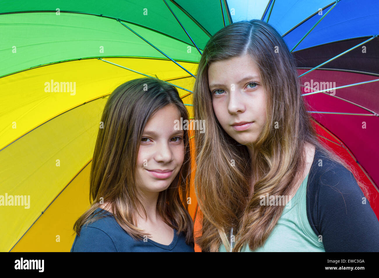 Zwei kaukasischen Teenager-Schwestern unter regenbogenfarbenen Regenschirm mit verschiedenen Farben Stockfoto