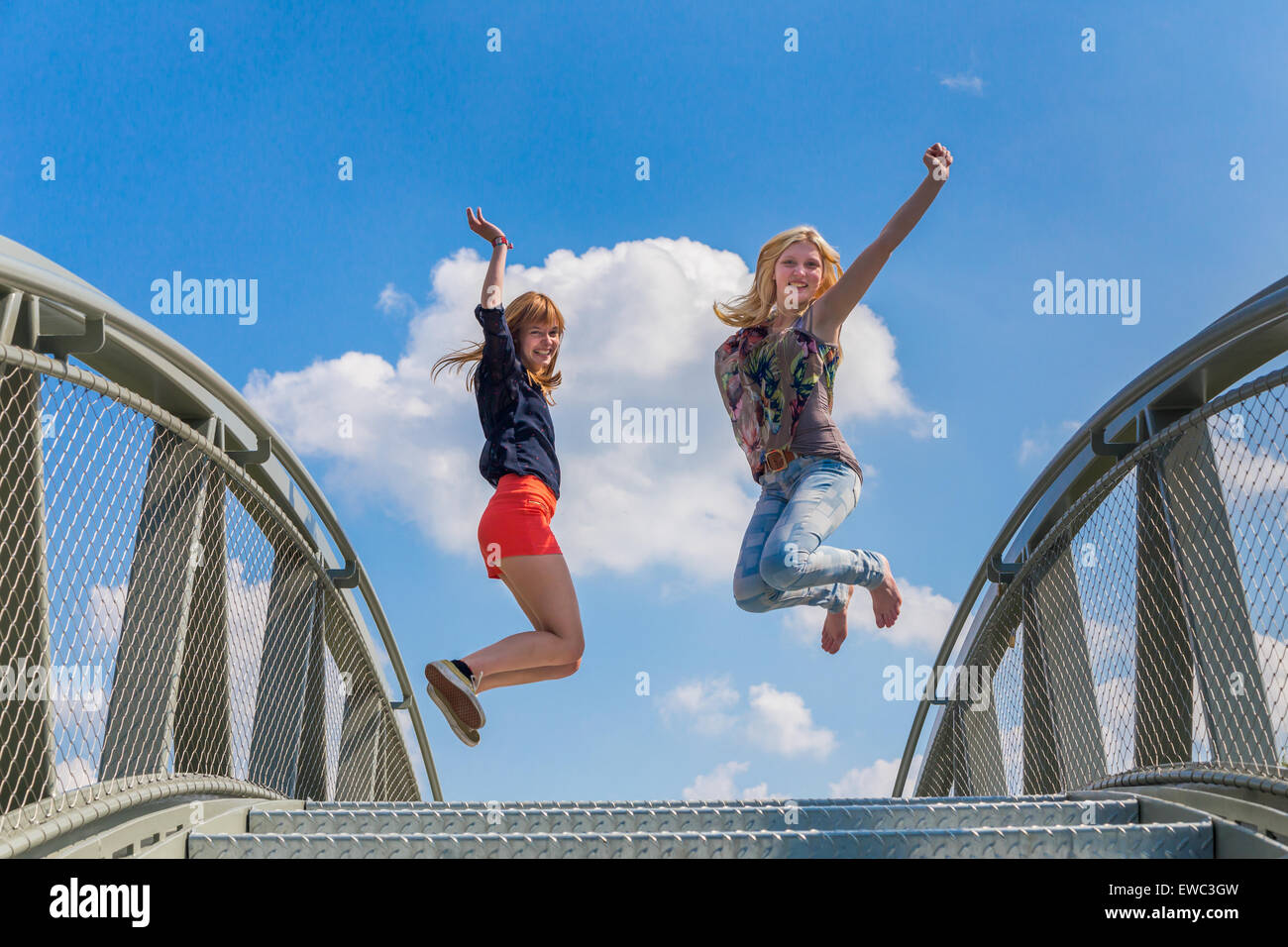 Zwei glücklich und begeistert Mädchen im Teenageralter auf Brücke vor blauen Himmel springen Stockfoto