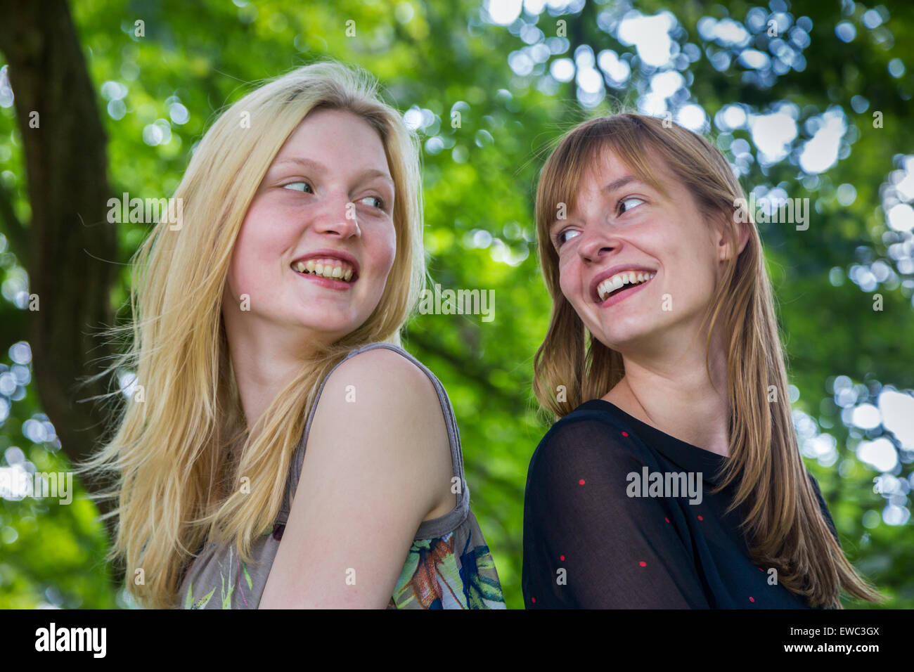 Zwei langhaarige holländische Mädchen im Teenageralter mit Baum Hintergrund miteinander Lachen Stockfoto