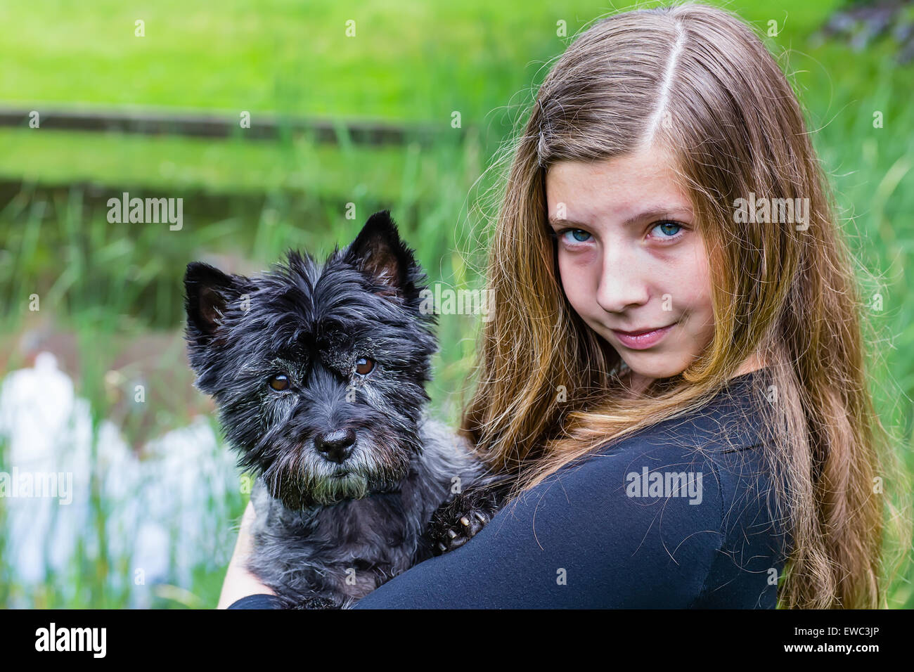 Blonde kaukasische Teenager-Mädchen tragen schwarzen Hund auf Arm im grünen park Stockfoto