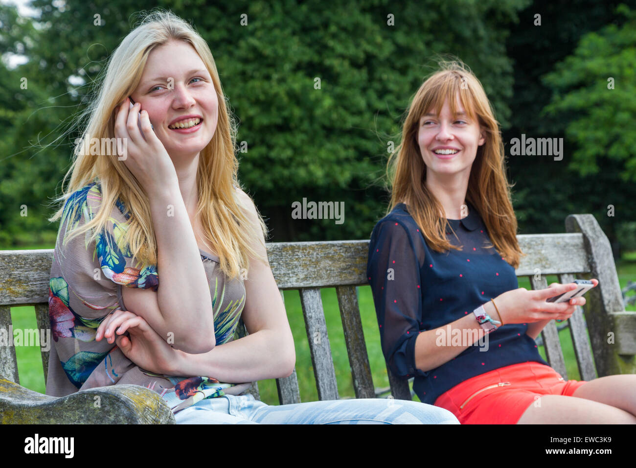 Zwei europäische Teenager Freundinnen sitzen auf der Bank im Park mit Handy Stockfoto