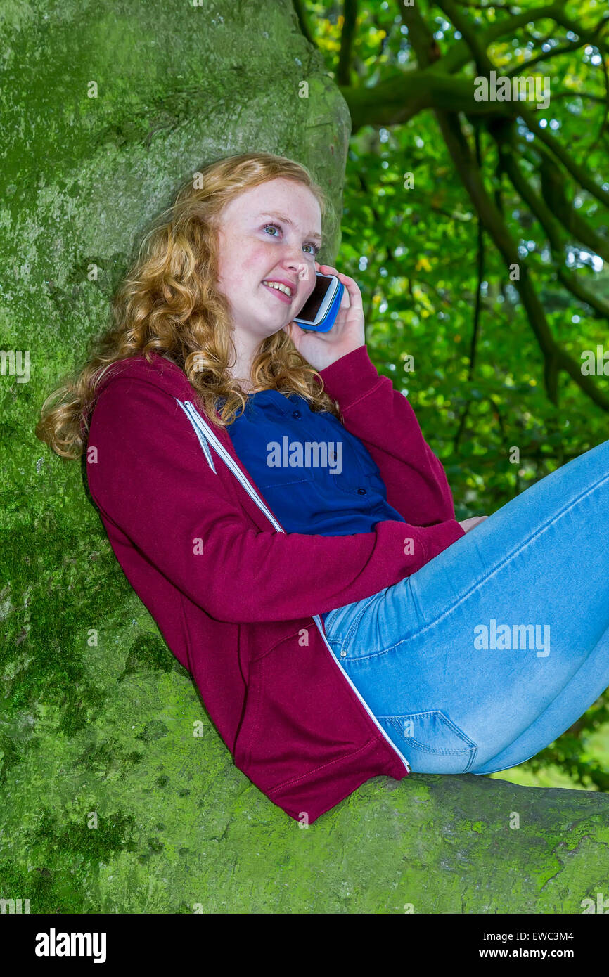 Teenager-Mädchen sitzen auf Baum aufrufen und lächelnd mit Handy Stockfoto