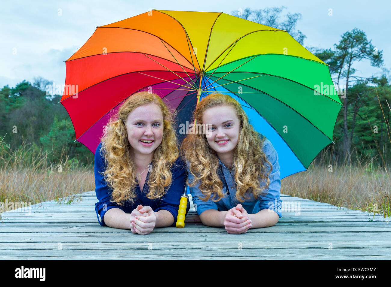 Zwei lächelnde kaukasischen Teenager Freunde liegen in der Natur unter bunten Regenschirm Stockfoto