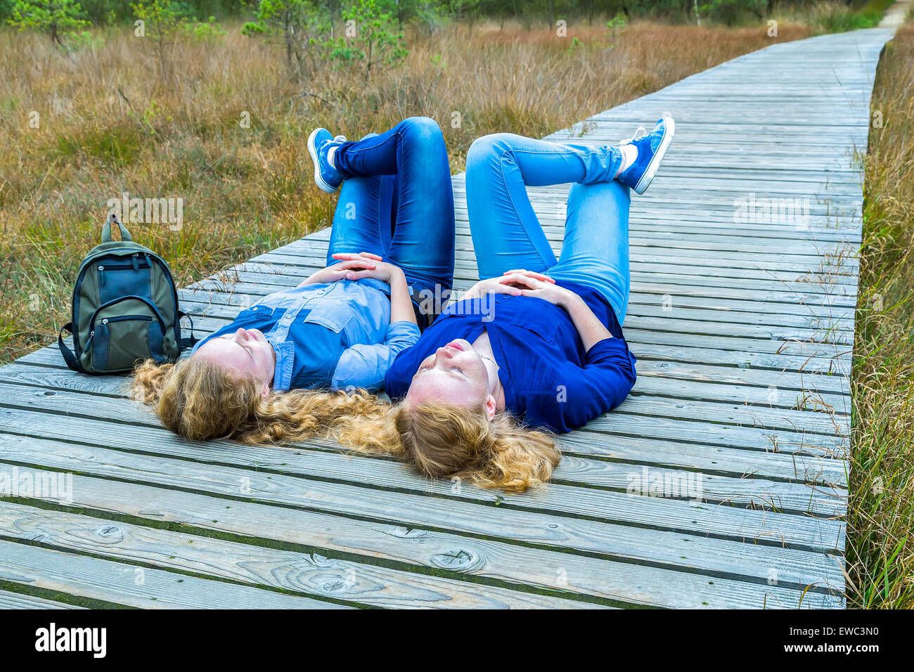 Zwei Mädchen im Teenageralter liegen auf dem Rücken am Holzweg in der Natur Stockfoto