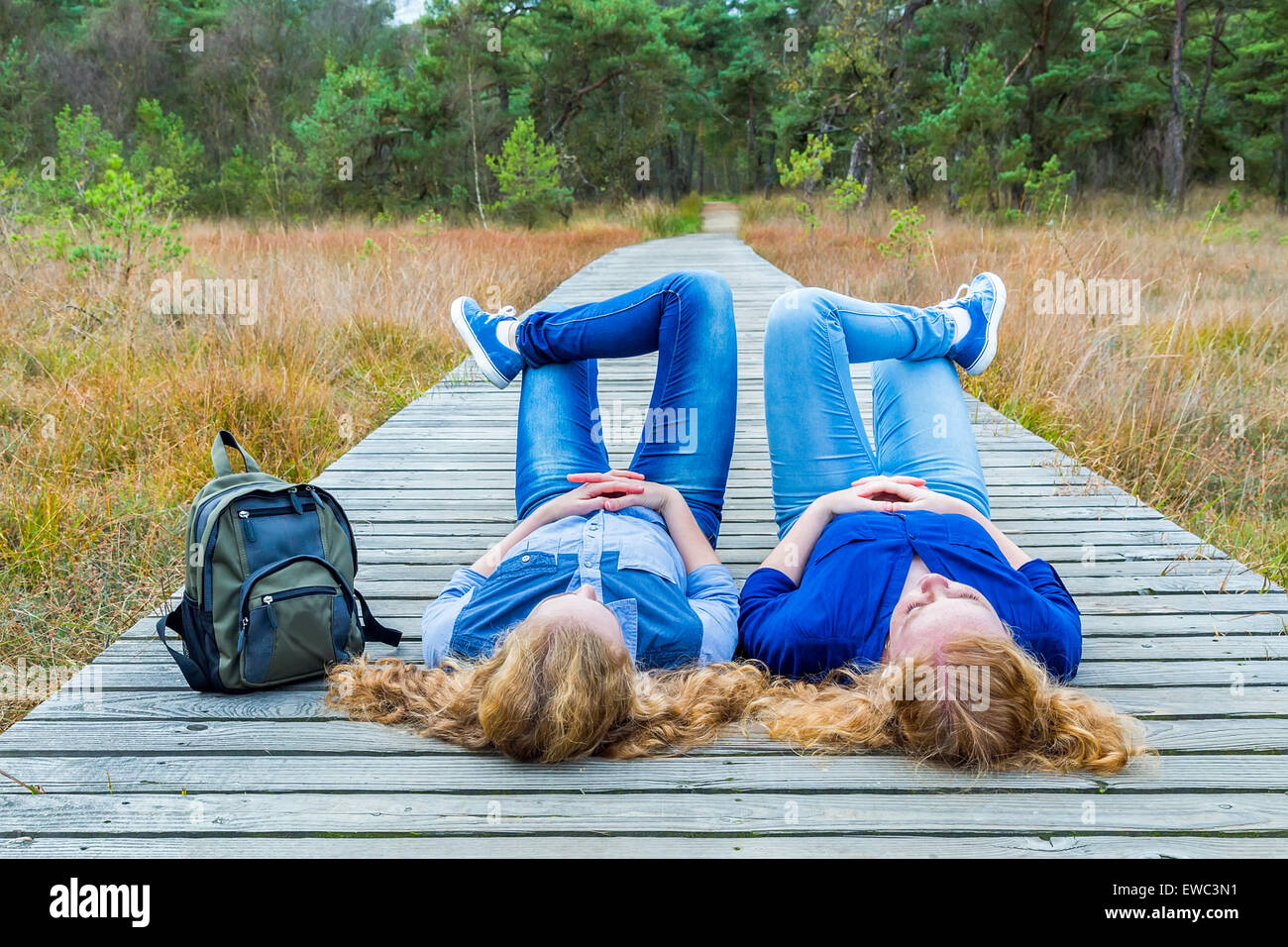 Zwei Mädchen im Teenageralter liegen auf dem Rücken auf hölzernen Fußweg in Natur Stockfoto