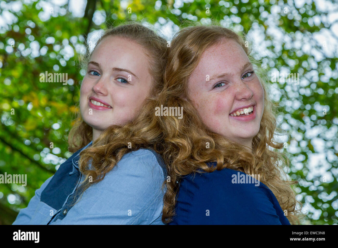 Zwei kaukasischen Teenager Schwestern Köpfe zusammen lachen unter grünen Baum Stockfoto