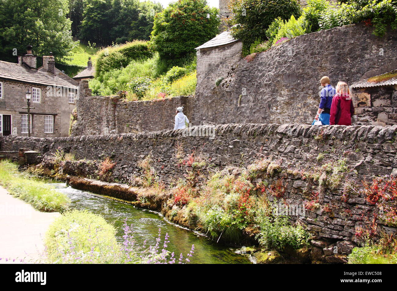 Wanderer passieren einer Trockensteinmauer auf Peakshole Wasser im Herzen von Castleton Dorf im Sommer Peak District Derbyshire UK Stockfoto